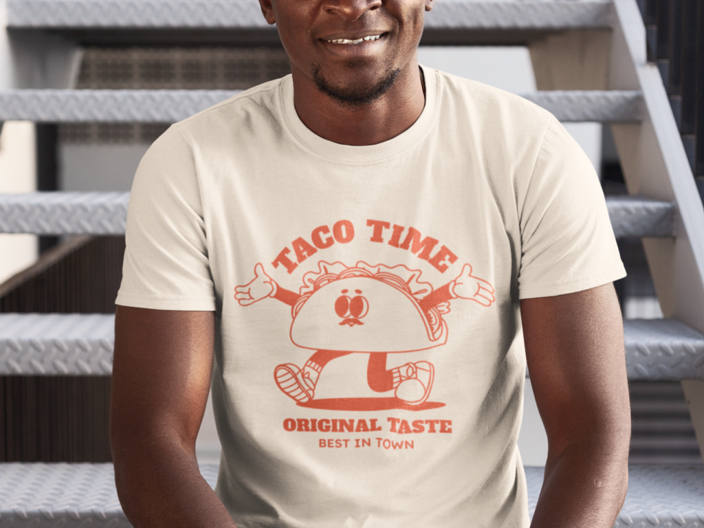 Man sitting on stairs wearing a light-colored t-shirt with a cheerful taco cartoon and text "Taco Time, Original Taste, Best in Town".