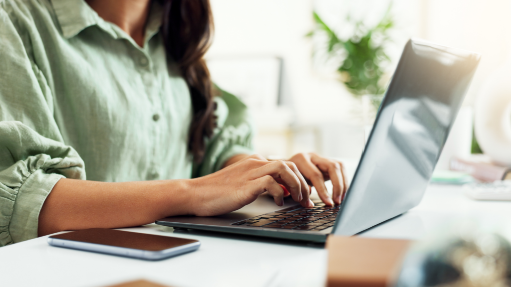 A woman in a green blouse sitting at a desk and using a laptop.