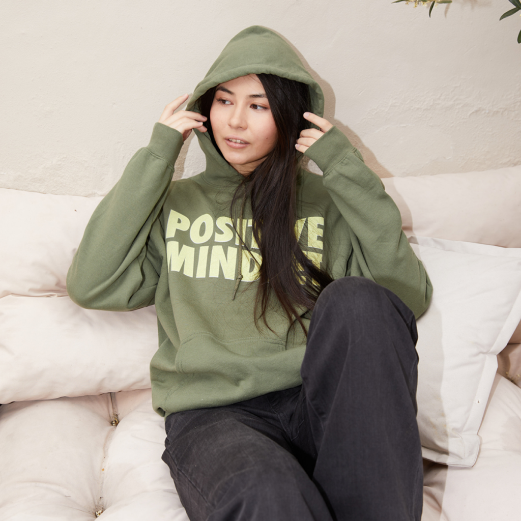 A woman in a custom “Positive Mindset” hoodie on a white couch.