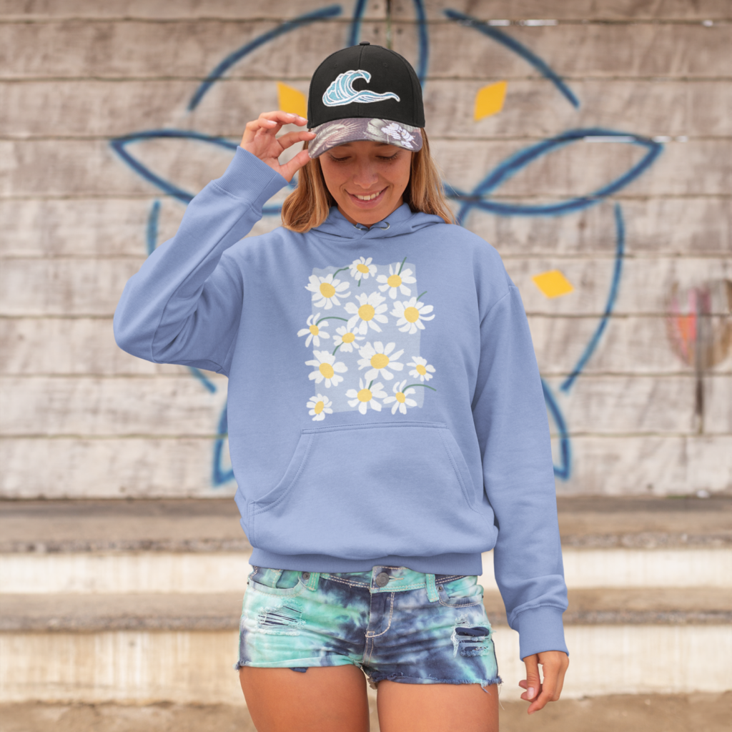 A woman in a trending blue hoodie with a floral print and denim shorts standing in front of a wall.