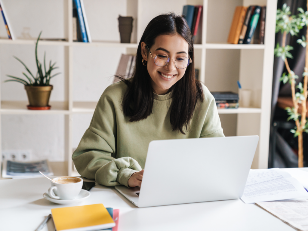 A woman smiles as she works on her laptop, excited about setting up her online store.