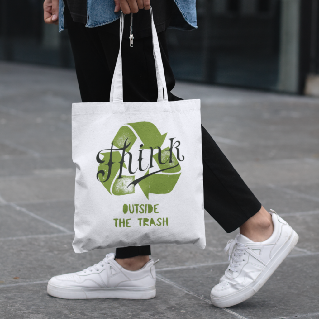 A person walking in the streets, wearing a custom “Think outside the trash” tote bag.