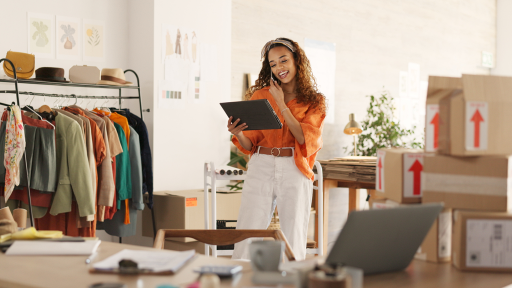 A woman stands before a desk cluttered with boxes and a laptop, engaged in her work environment.